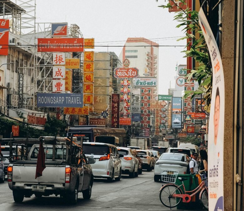 Vibrant street view of Bangkok's Chinatown with colorful signs and traffic, showcasing urban life.